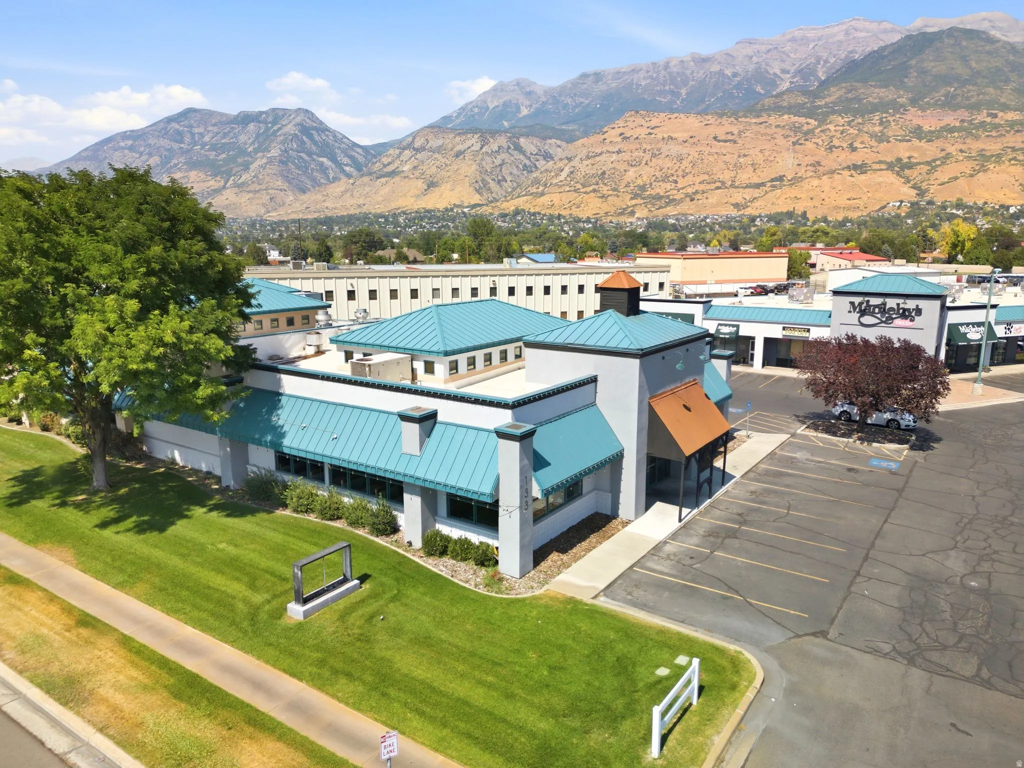 Modern commercial facility featuring distinctive turquoise metal roofing, clean-lined architectural design, and expansive paved parking area