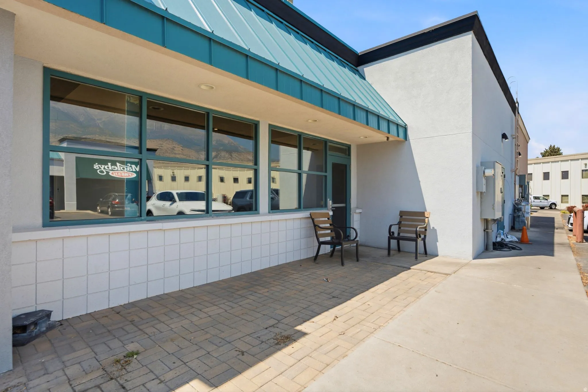 Modern commercial storefront featuring expansive glass entry doors and transom windows, white tile wainscoting, paved patio area with integrated seating, and clean architectural lines with contemporary roofline detailing