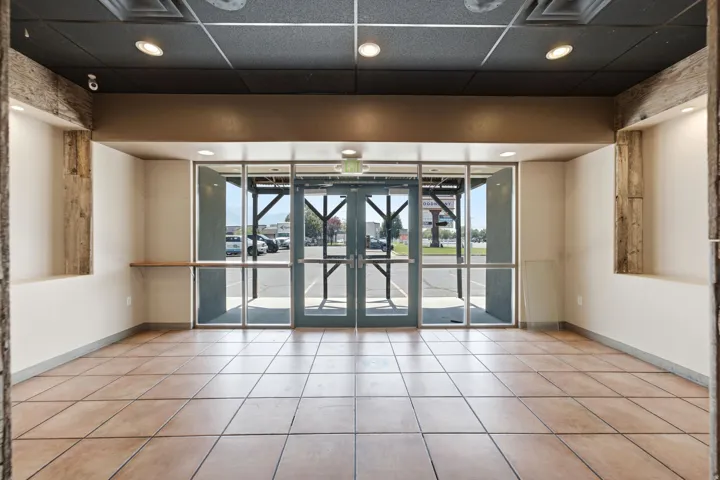 Full-height glass entry doors, recessed lighting, neutral tile flooring, and exposed wood beam accents