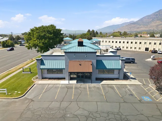 Building exterior featuring a multi-tone facade, teal metal roofing, multiple windows, and an integrated parking lot