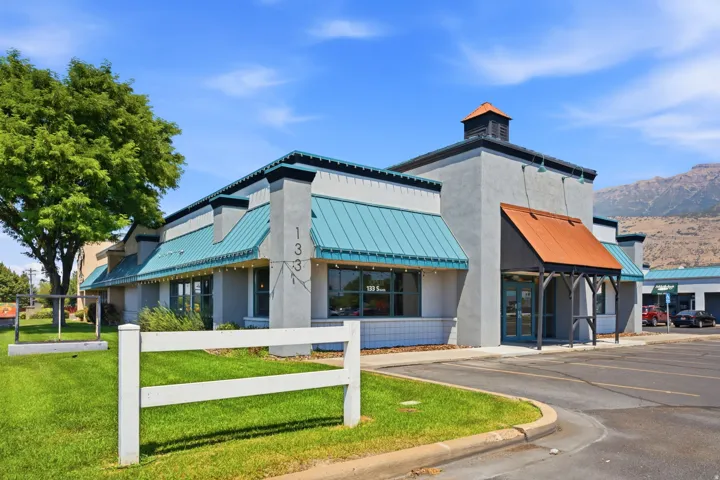Modern commercial or mixed-use building featuring a striking contemporary design with turquoise and orange metal awnings, clean concrete facade, and cupola-style roof element