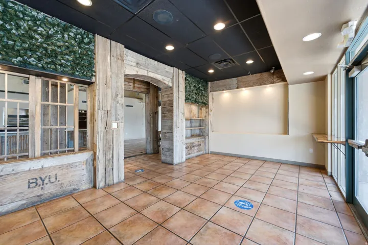 Spacious retail or commercial interior featuring terracotta tile flooring, recessed ceiling lighting, and large front-facing windows with natural light