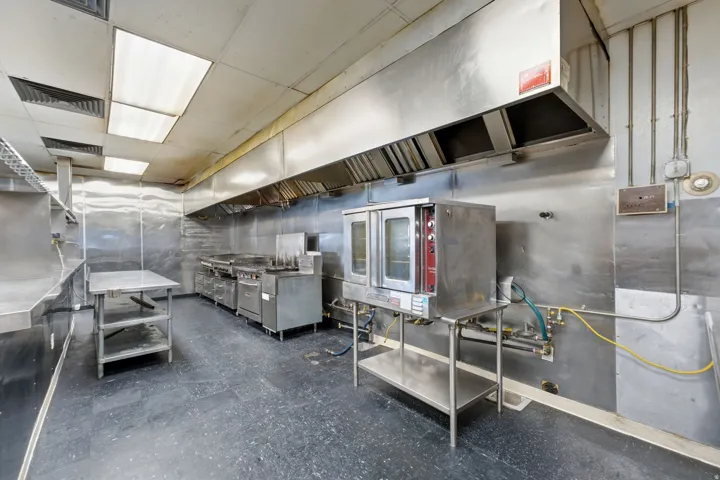 Commercial kitchen featuring stainless steel equipment, expansive exhaust hood system, and durable flooring