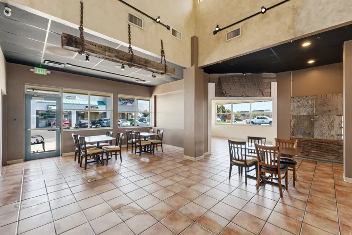 Spacious commercial or multi-use interior featuring polished tile flooring, abundant natural light from expansive storefront windows, exposed ceiling with recessed lighting, and structural support columns