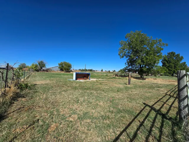 Expansive outdoor space featuring a wire fence, wood fence posts, mature trees, and a small shelter