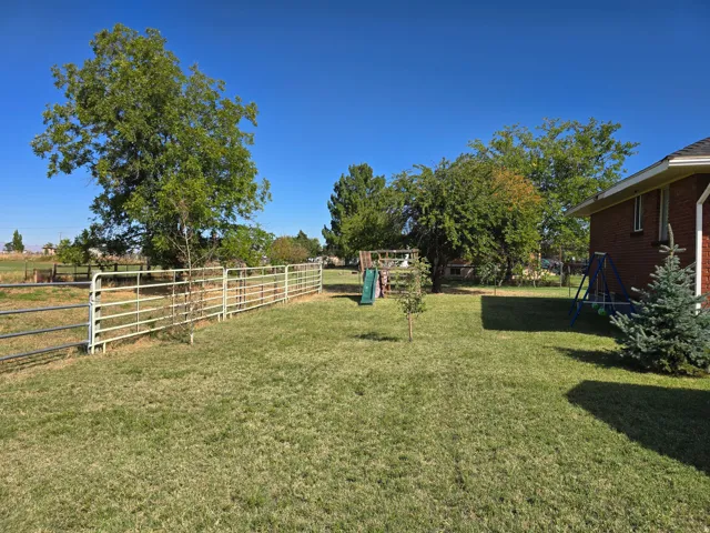 Expansive grass lawn featuring mature trees and a metal perimeter fence
