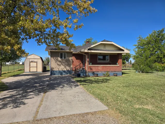 Brick exterior with siding addition, covered front porch, concrete driveway, detached storage shed, and a grassy lawn