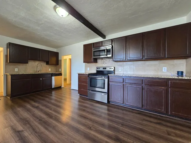 Kitchen featuring wood-finish flooring, dark wood cabinetry, light-toned tiled backsplash, and stainless steel appliances