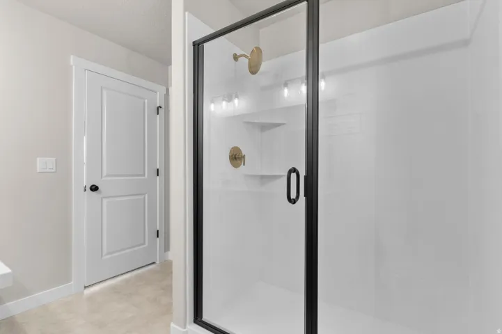 Glass-enclosed shower with a black frame and hardware, featuring a gold-toned showerhead and fixtures