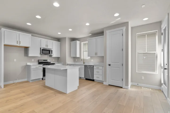 Modern kitchen featuring light wood-finish flooring, white cabinetry, stainless steel appliances, and recessed lighting