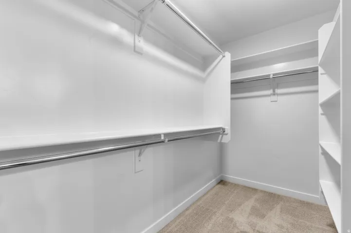 White painted walls, carpet flooring, multiple chrome hanging rods, and built-in shelving