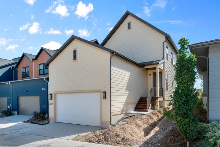 Cream-colored siding exterior, attached two-car garage, dark trim accents, covered entry porch, and exterior lighting fixtures