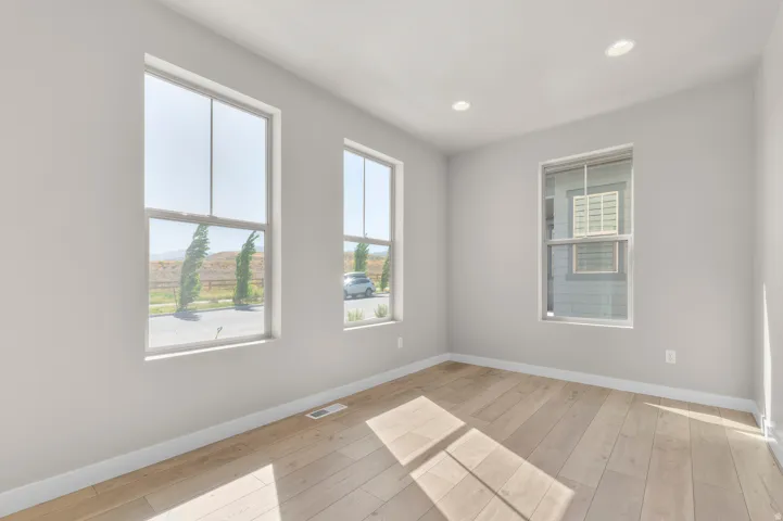 Light-filled room featuring three windows, recessed ceiling lighting, and wood-finish flooring