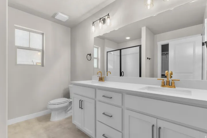 Dual vanity with gold-finish faucets and undermount sinks, white cabinetry with silver-tone hardware, and a large mirror