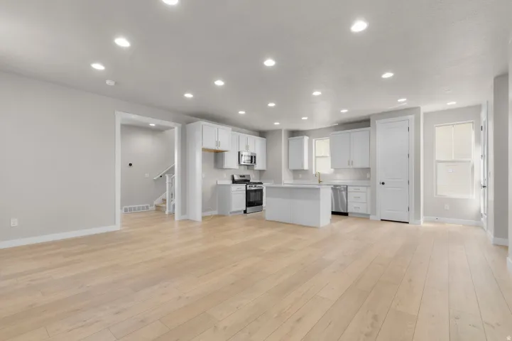 Open-concept living area with light wood-finish flooring, recessed lighting, and a kitchen featuring white cabinetry, a center island, and stainless steel appliances