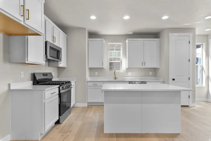 Kitchen featuring white cabinetry, gold-tone hardware, stainless steel appliances, a center island, and wood-finish flooring