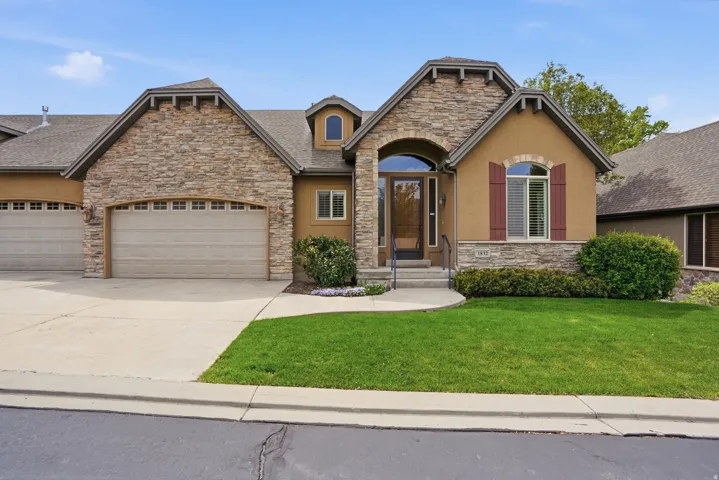 Stucco and stone facade with arched entry, multi-pane garage doors, and landscaped front yard with a walkway