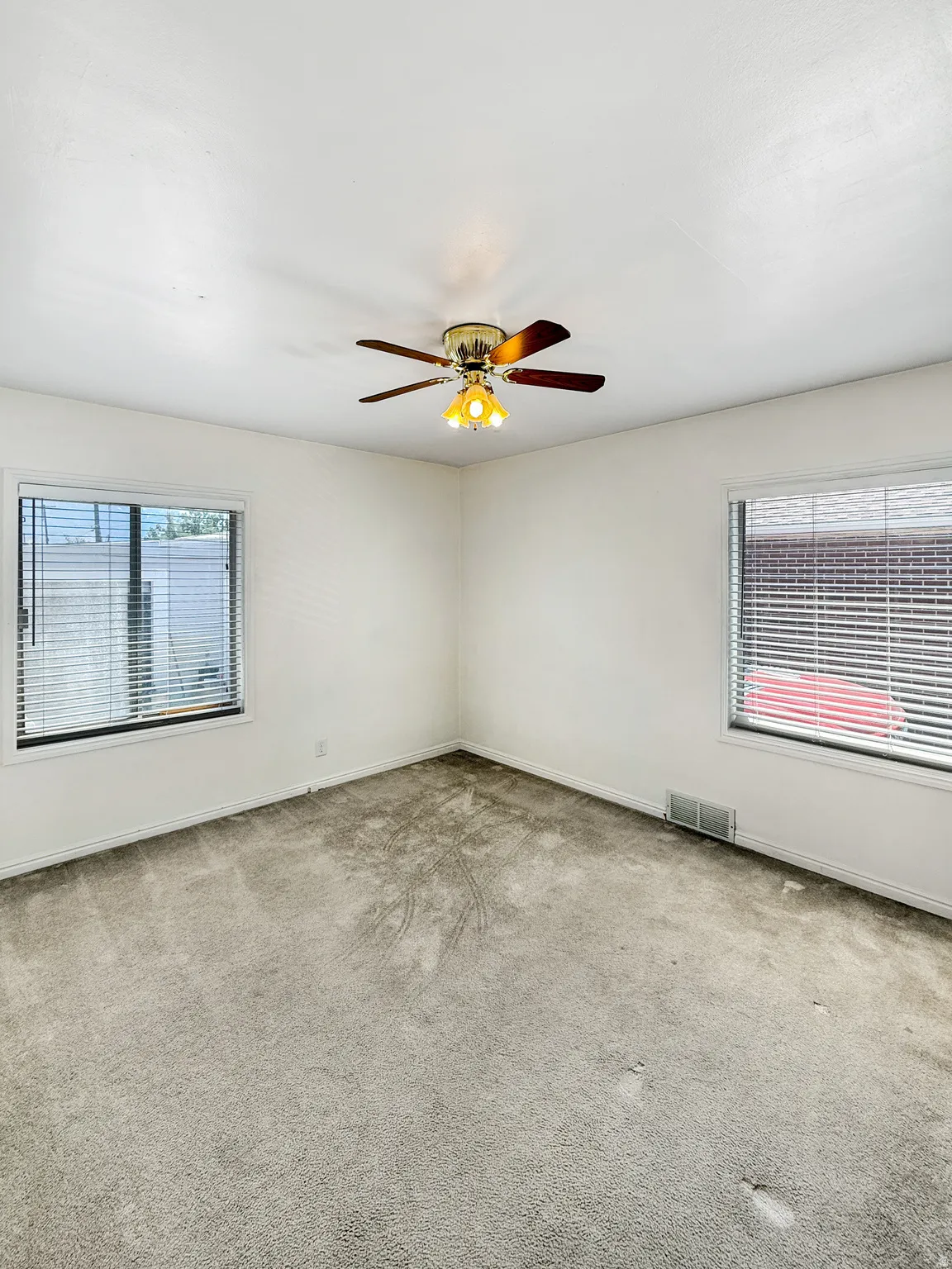 Light-filled room featuring neutral wall paint, two windows with blinds, a ceiling fan with integrated lighting, and carpeted flooring