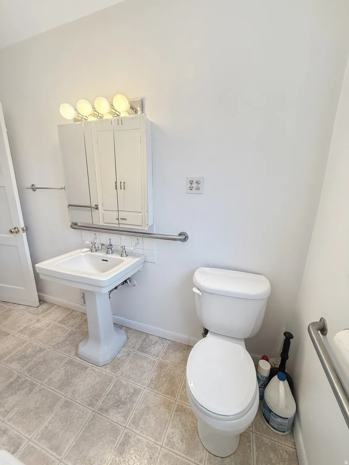 Pedestal sink with white tile backsplash, chrome fixtures, and overhead vanity lighting