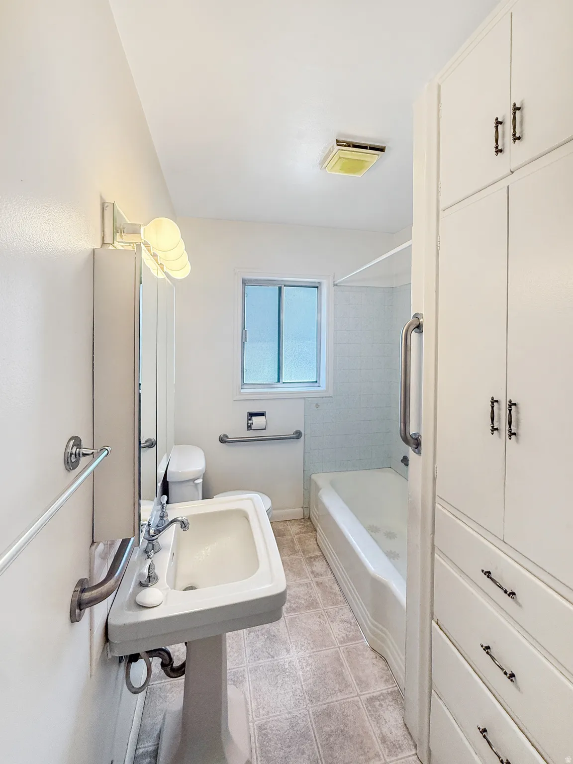 Bathroom featuring a pedestal sink, white cabinetry with dark hardware, a full bathtub with a shower, and a privacy window