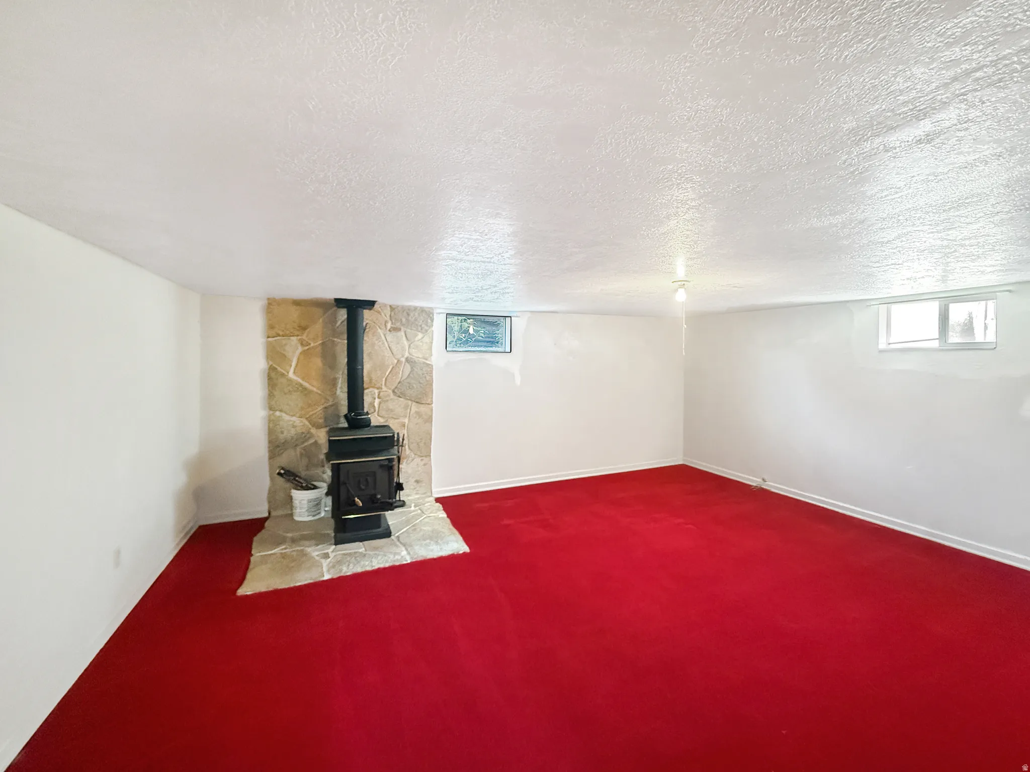 Spacious recreation room featuring vibrant red carpeting throughout, complemented by a black wood-burning stove with stone surround and hearth