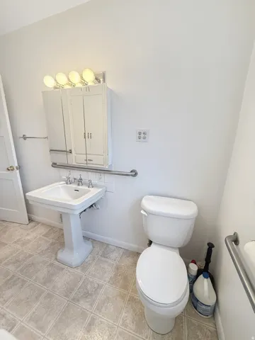 Pedestal sink with white tile backsplash, chrome fixtures, and overhead vanity lighting