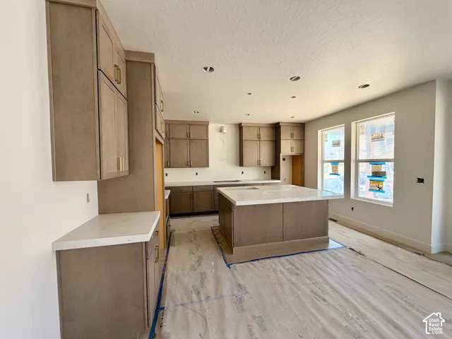 Expansive kitchen featuring a large central island, extensive cabinetry with gold-tone hardware, and light-toned countertops