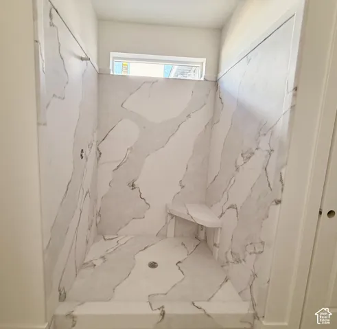 Shower enclosure featuring marble-look wall panels, a built-in corner bench, a window, and a floor drain