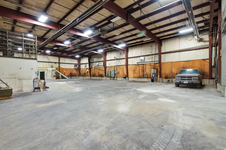 Expansive warehouse space featuring concrete flooring, exposed metal beam construction, skylights, and fluorescent lighting fixtures