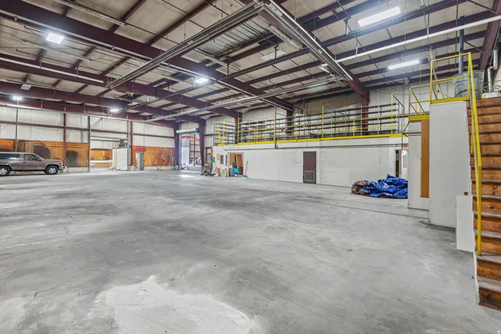 Expansive concrete flooring throughout, high ceilings with exposed metal framework, and multiple overhead lighting fixtures