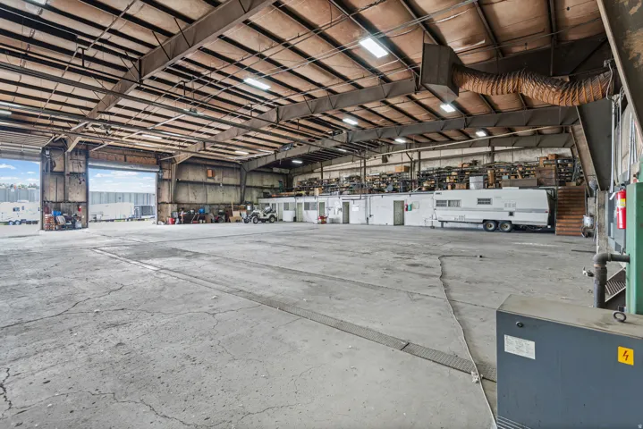Spacious warehouse interior featuring high ceilings, exposed structural beams, concrete flooring, and multiple large roll-up doors