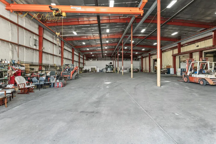 Expansive industrial warehouse featuring a concrete floor, exposed metal beam ceiling, overhead gantry crane, and fluorescent lighting