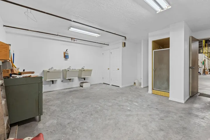 Concrete flooring, multiple utility sinks, enclosed shower, and white bi-fold doors