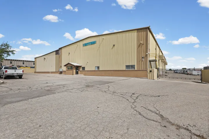 Expansive paved lot with a large industrial building, featuring a gated entry, security booth, and a secondary structure