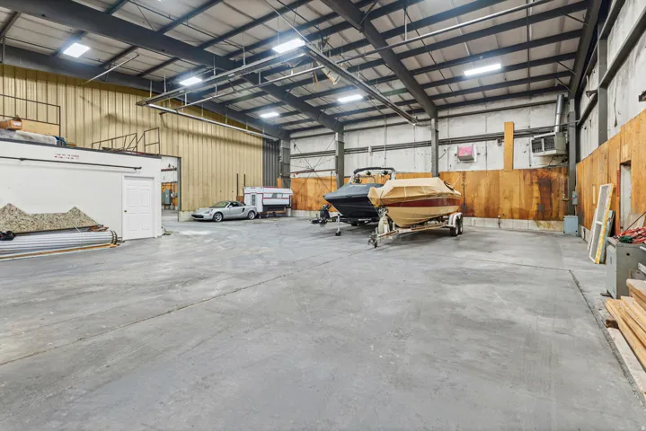 Spacious warehouse with expansive concrete flooring, industrial-grade metal roof structure with integrated lighting, and ample clearance for equipment storage and vehicle parking