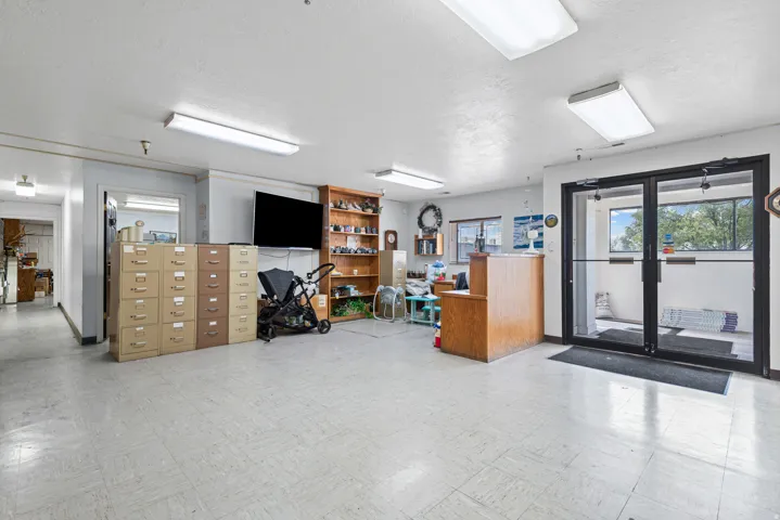 Spacious commercial or office space featuring polished concrete flooring, recessed and linear ceiling lighting, built-in wood cabinetry and storage units, and glass-panel entry doors with natural light from multiple windows