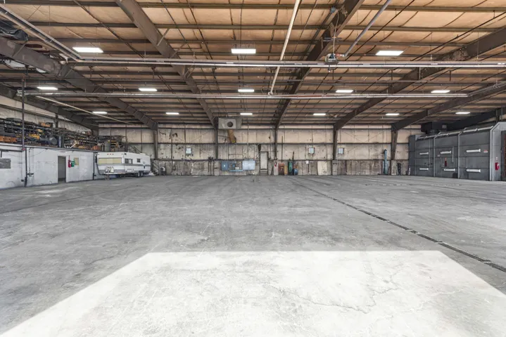 Expansive warehouse space featuring a high ceiling, concrete flooring, exposed structural beams, and integrated overhead lighting