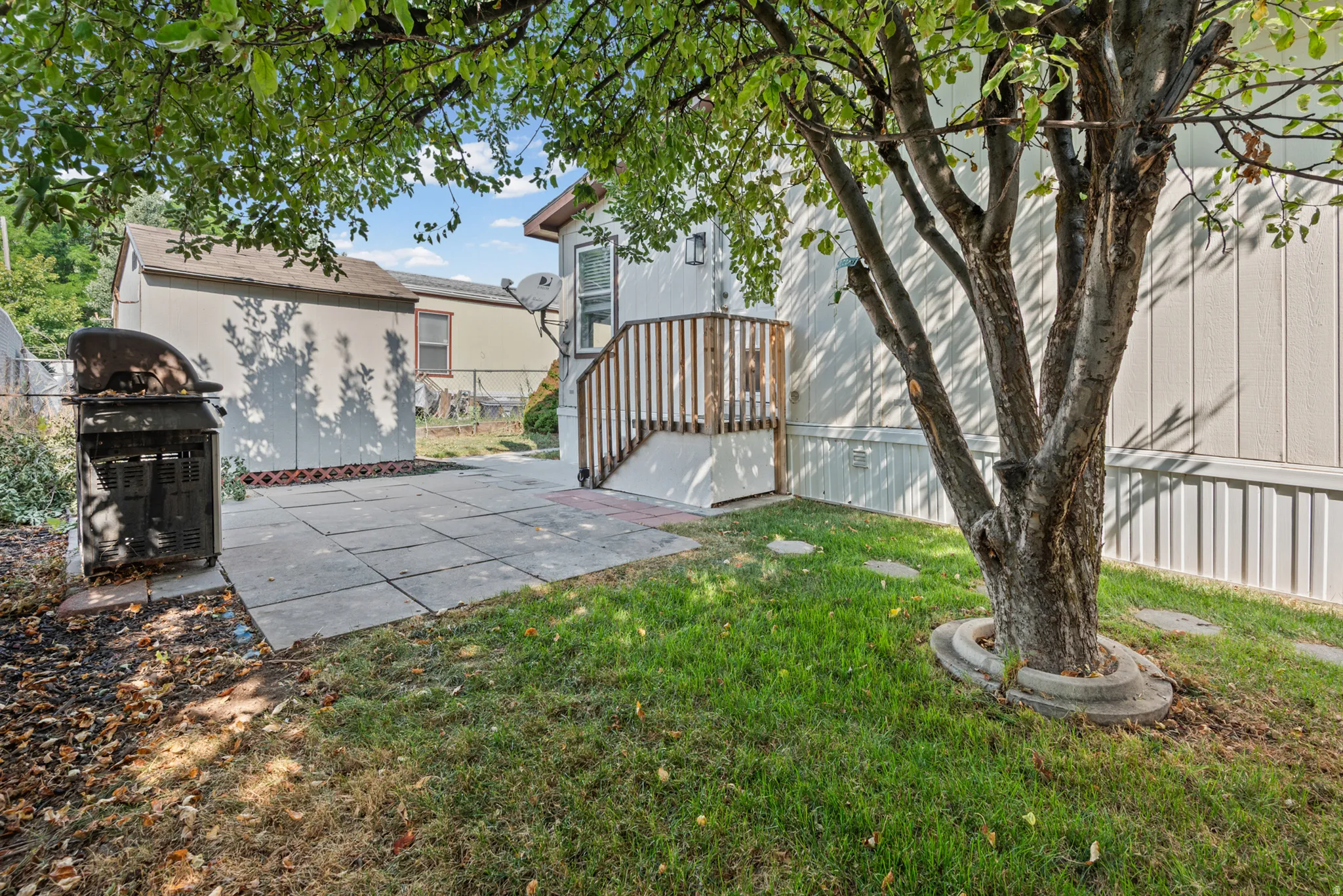Patio area with concrete pavers, green lawn, mature trees, and wooden deck with railings