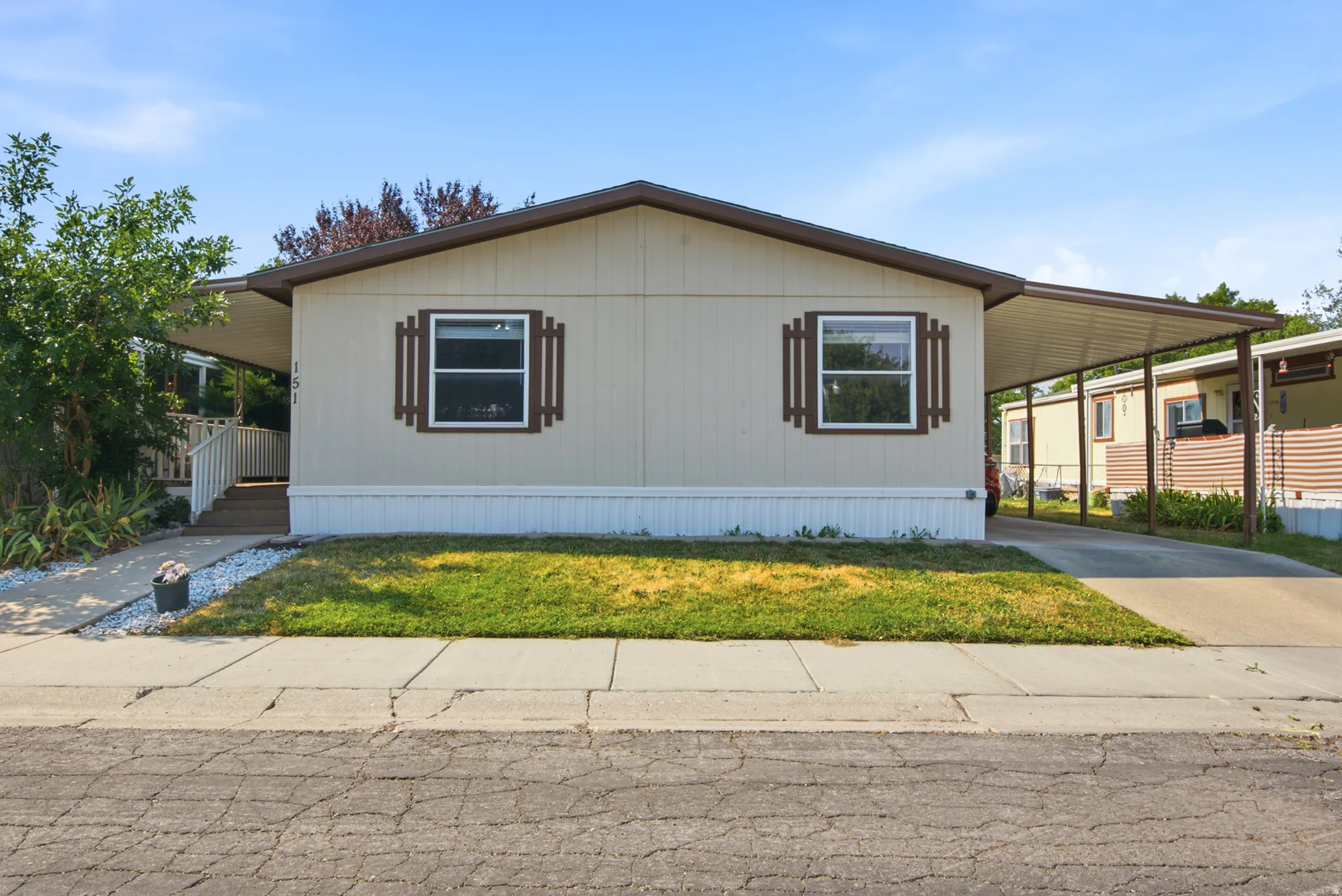 Front elevation with a covered entryway, attached carport, and a light-toned exterior with dark trim