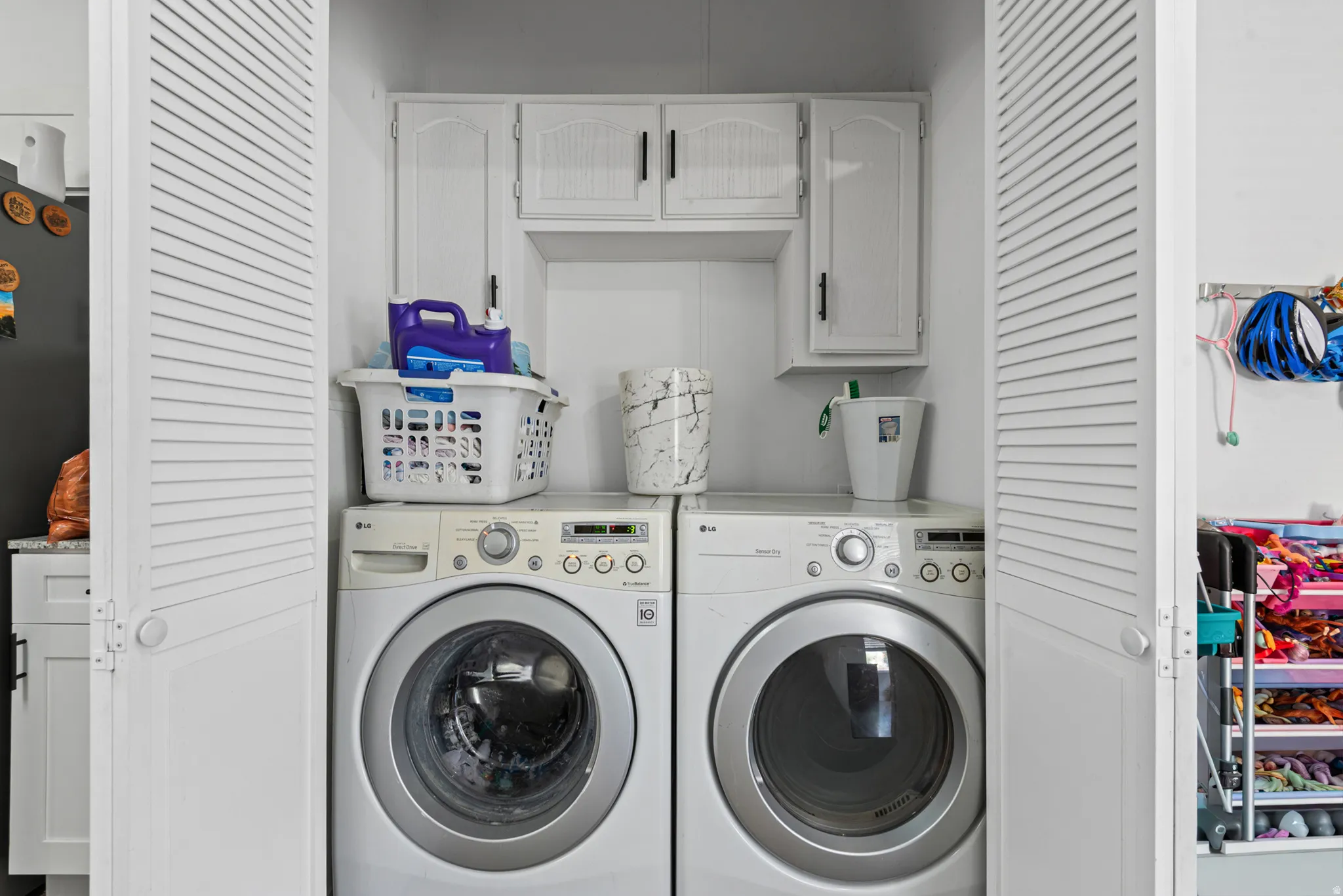 Dedicated laundry area with upper cabinetry and louvered bifold doors