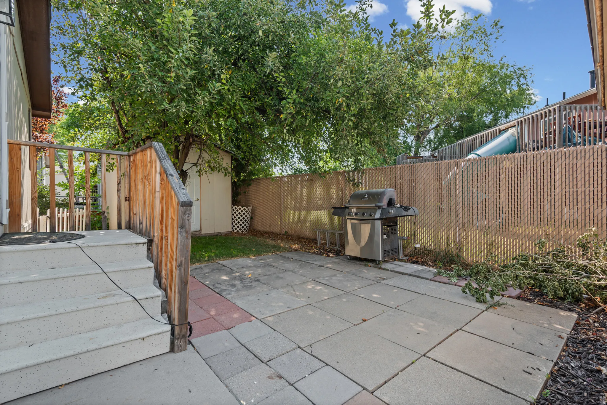 Paved patio area with a privacy fence, exterior steps, and mature landscaping