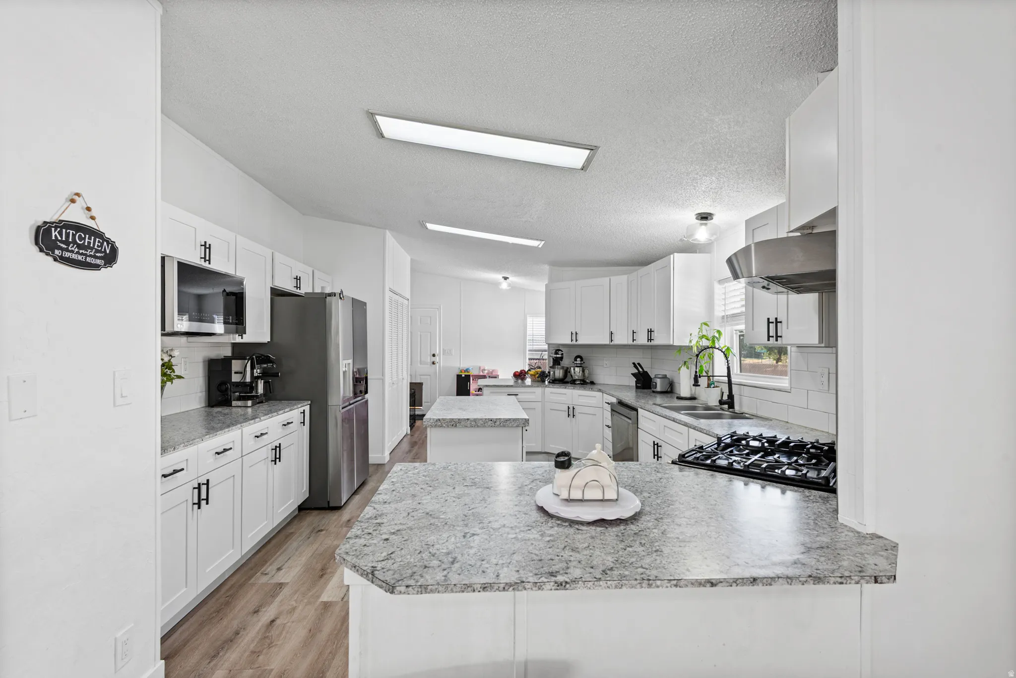 White cabinetry with dark hardware, stainless steel appliances, wood-finish flooring, and subway tile backsplash