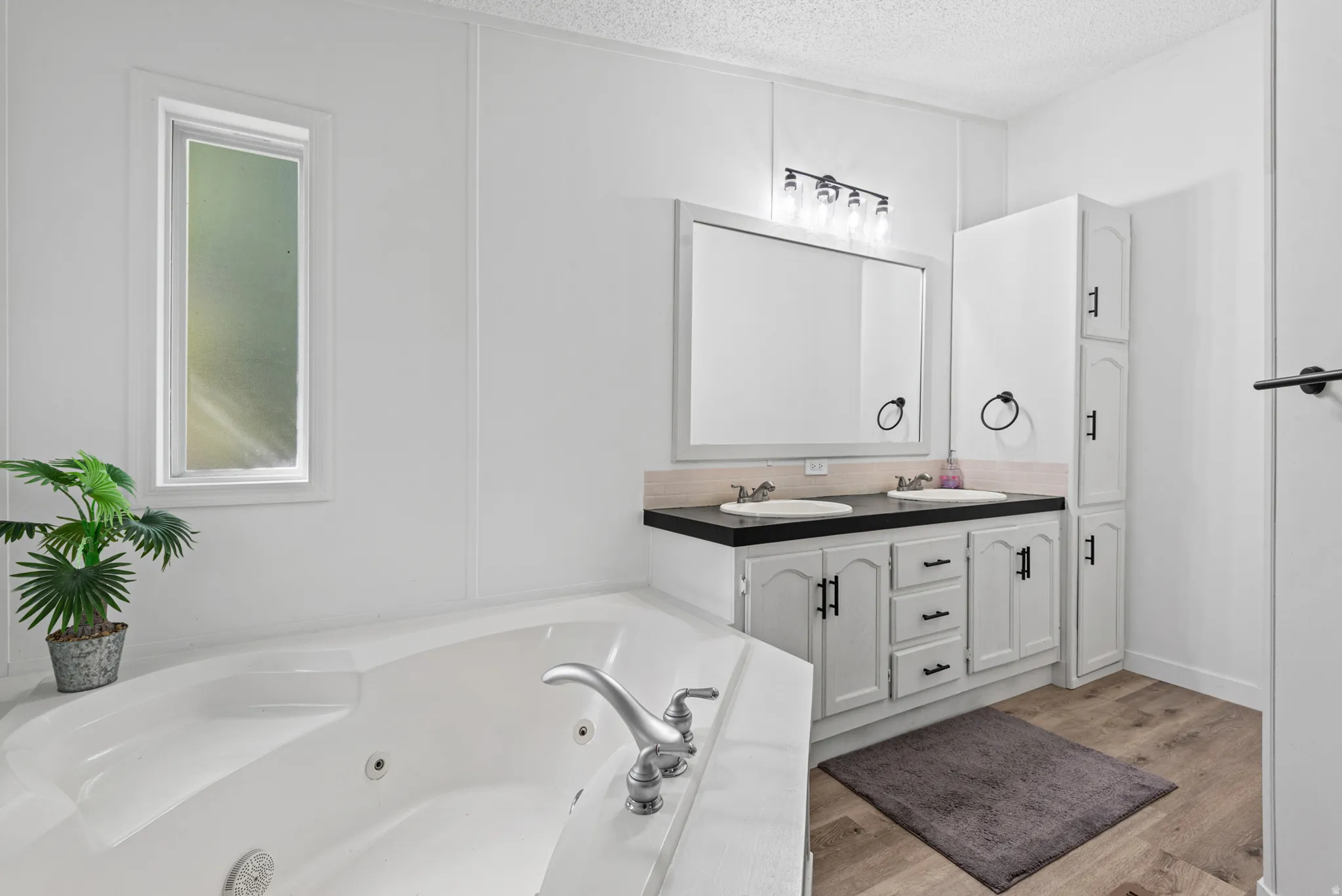 Master bedroom's bathroom - White jetted soaking tub, dual vanity with undermount sinks, black countertops, and wood-finish flooring