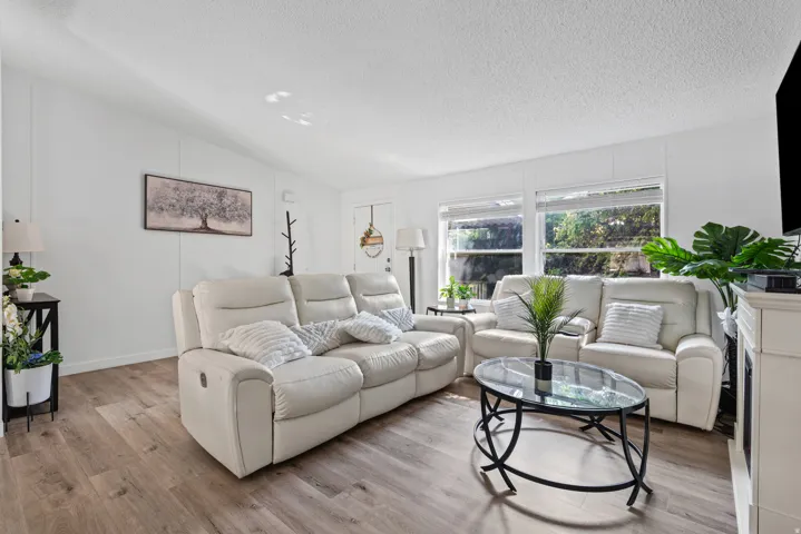 Wood-finish flooring throughout, white wall paneling, multiple windows with blinds, and recessed lighting