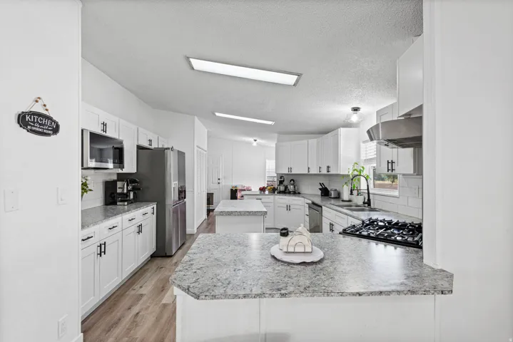 White cabinetry with dark hardware, stainless steel appliances, wood-finish flooring, and subway tile backsplash