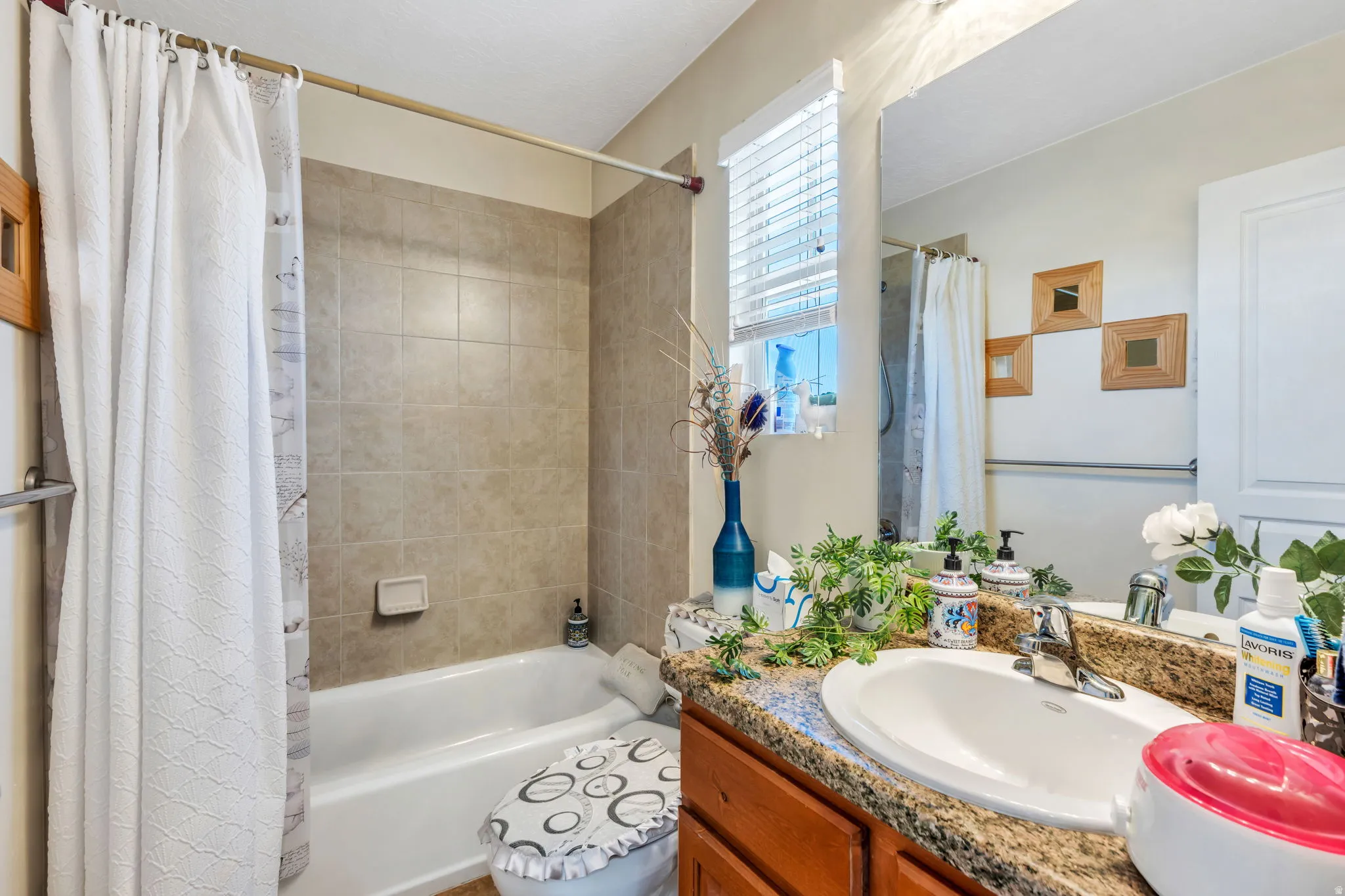 Bathroom featuring a white bathtub, tiled shower surround, wood-finish vanity with an integrated sink, and a framed mirror