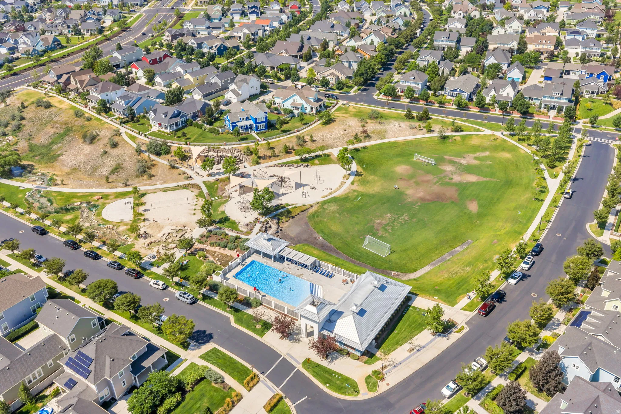 Community recreational area featuring a swimming pool, expansive green space, paved pathways, and sand play areas