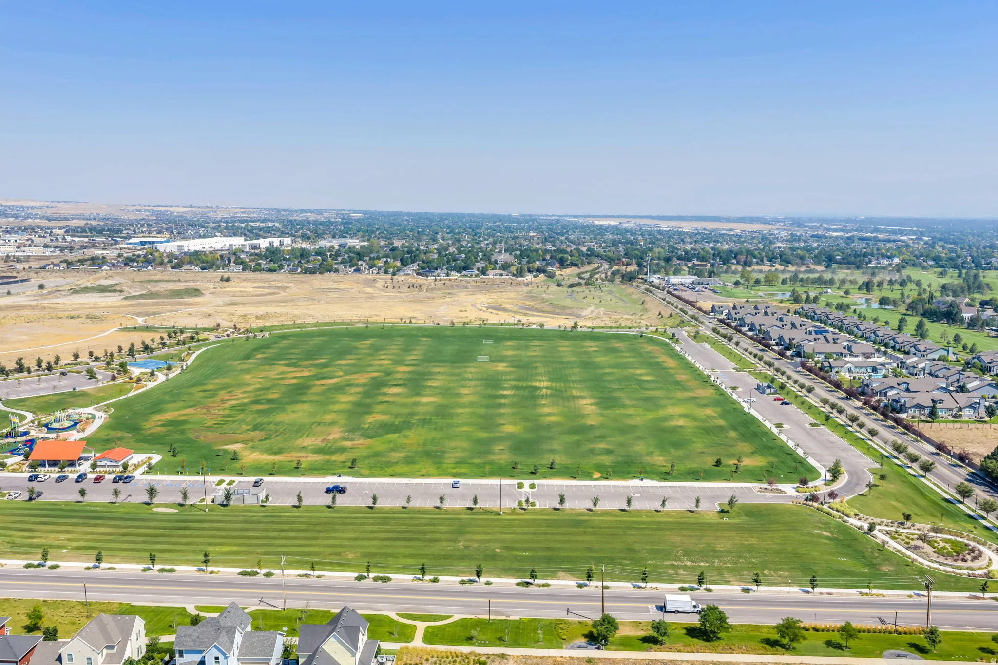 Expansive green spaces featuring a large sports field, adjacent residential area, and distant urban landscape