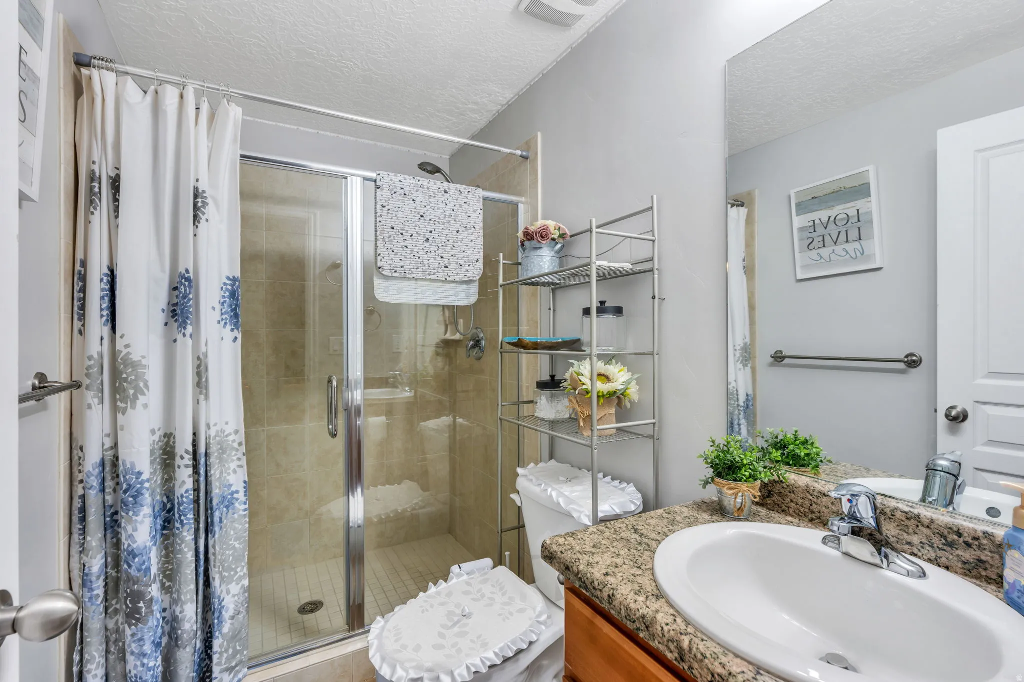 Glass-enclosed shower with tiled walls and floor, vanity with an integrated sink, granite-style countertop, and a large wall-mounted mirror