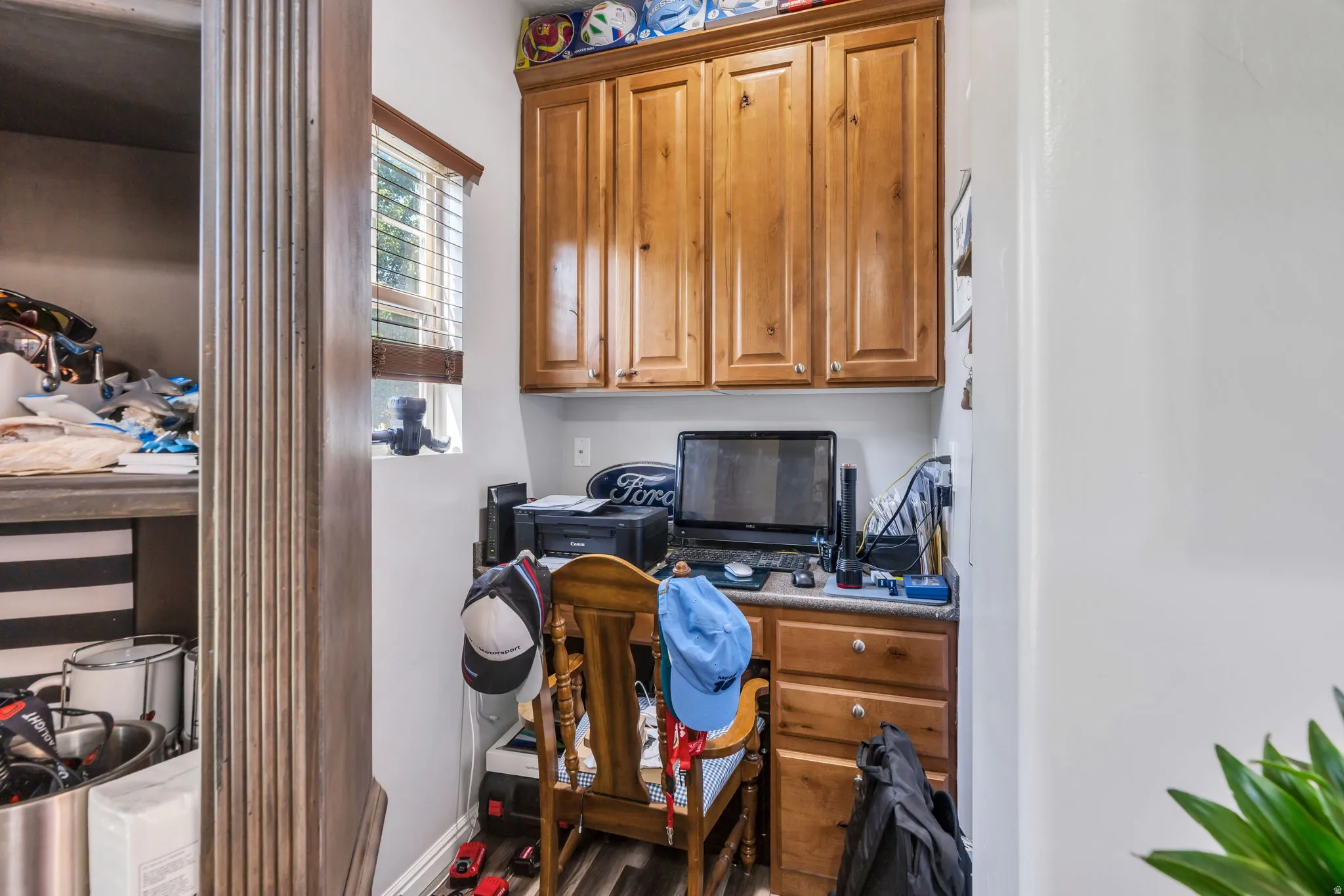 Built-in desk with wood-finish cabinetry, upper storage cabinets, and wood-finish flooring